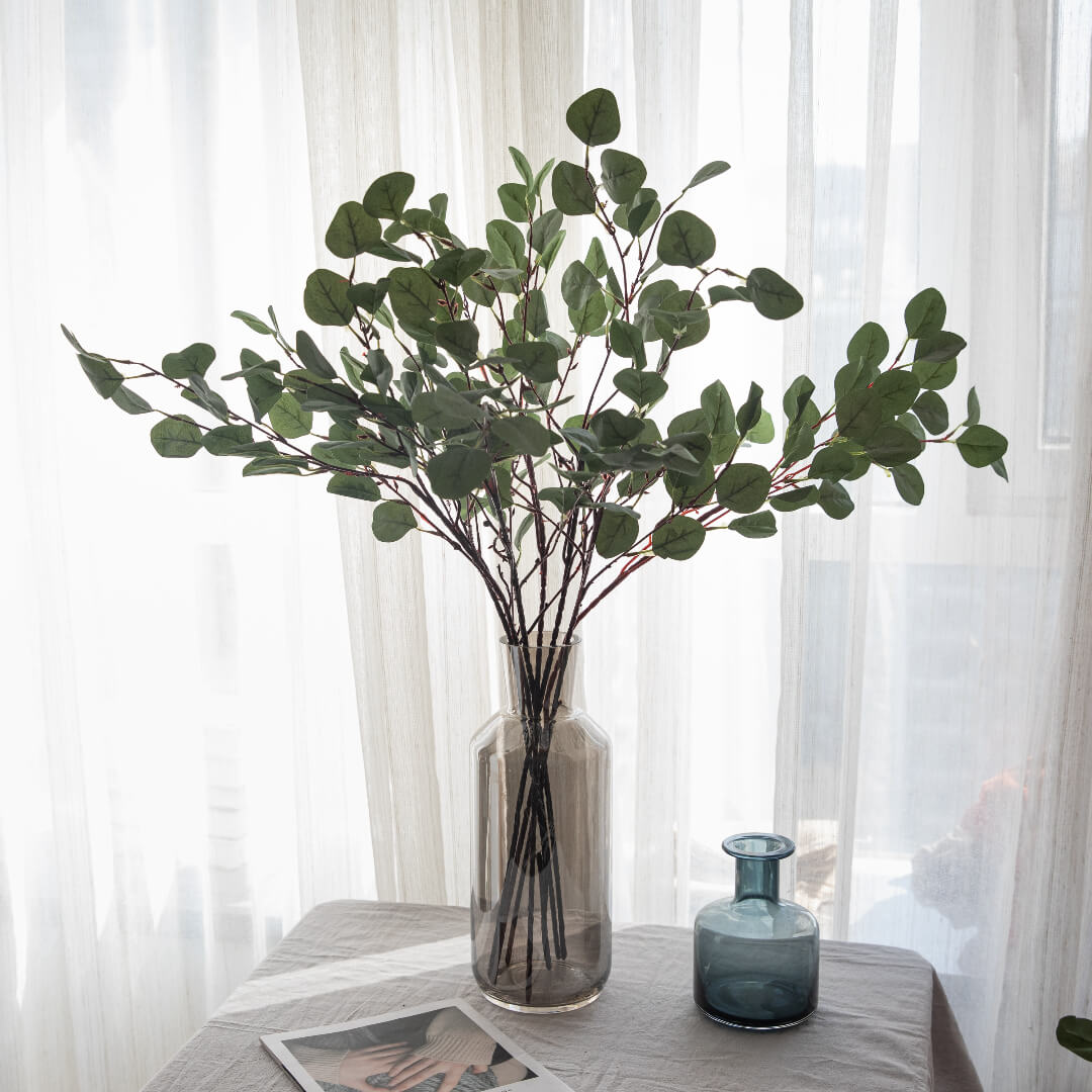 Eucalyptus branches in a vase in lush greenery.