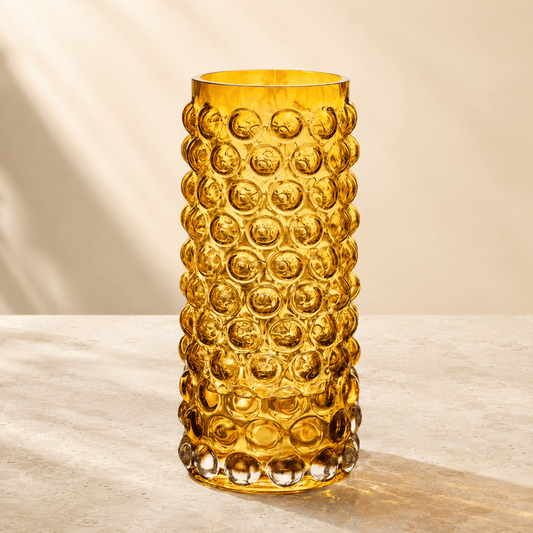 Amber tall bubble glass vase with raised circular texture on a warm ivory stone surface