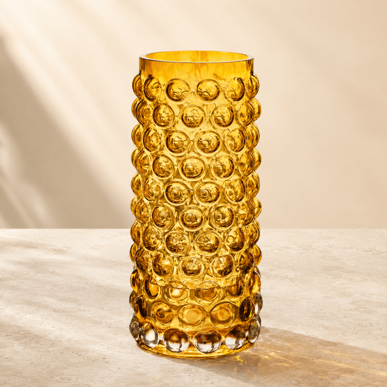 Amber tall bubble glass vase with raised circular texture on a warm ivory stone surface