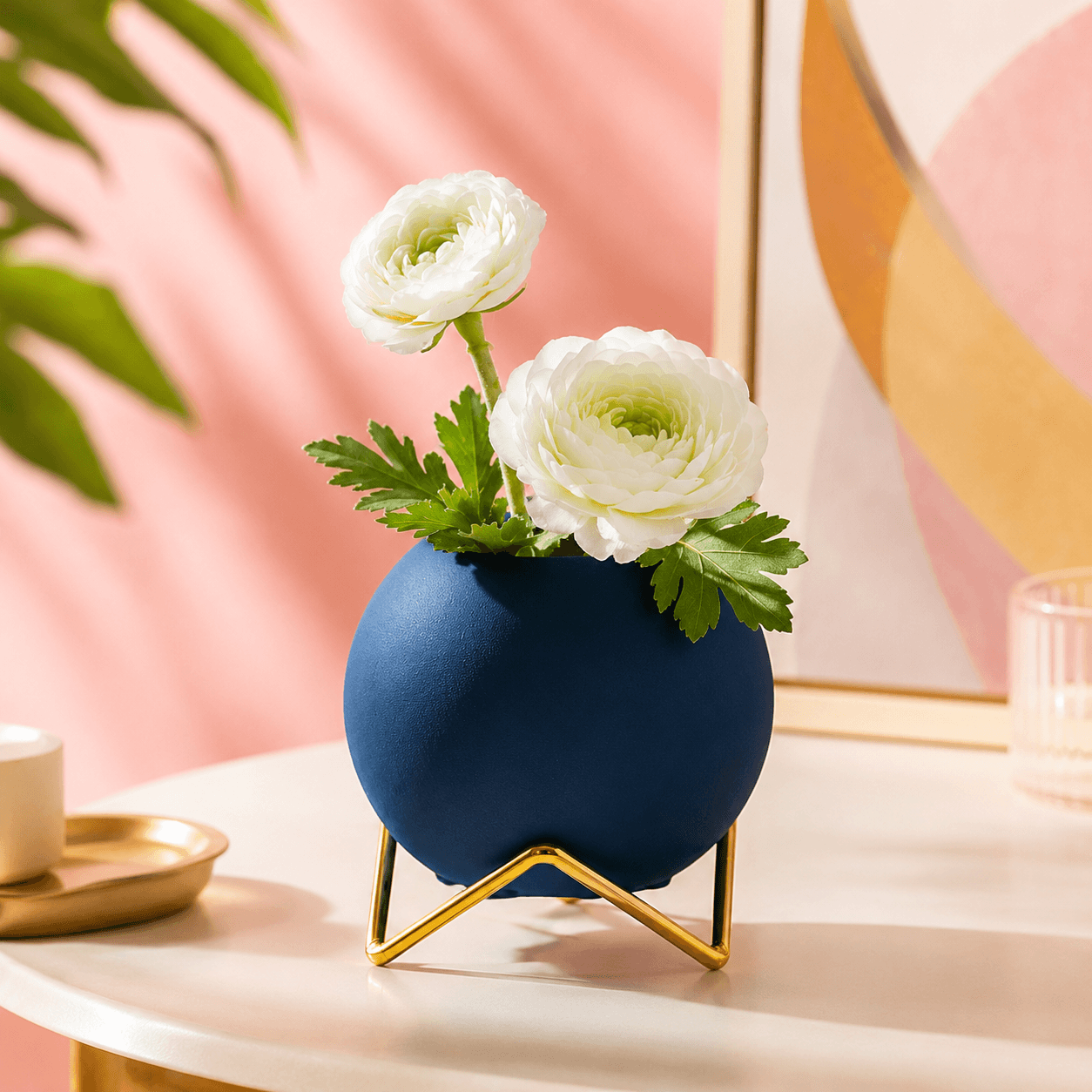 Blue round vase with gold stand and white flowers on a bright tabletop