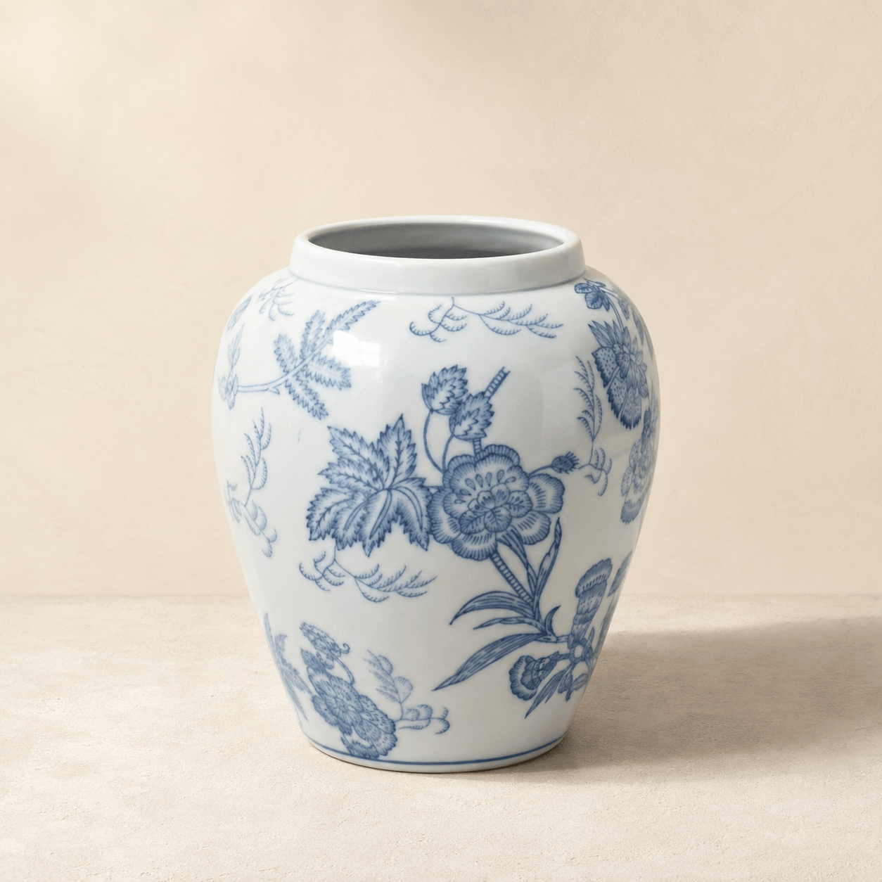 Blue and white botanical ceramic vase with a rounded urn shape on a warm ivory background