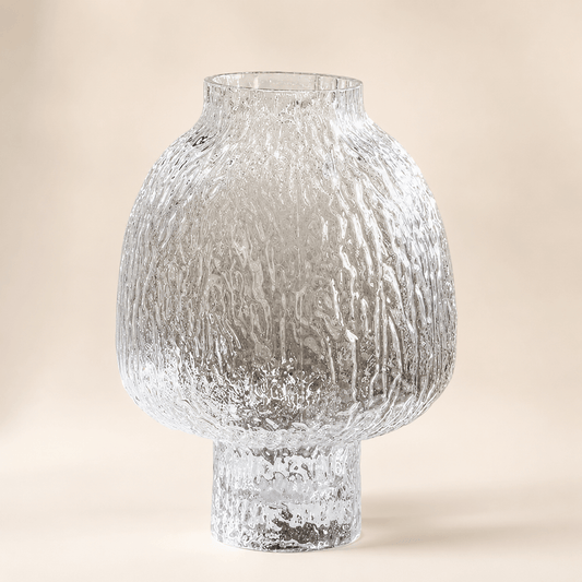 Clear textured glass vase with a rounded lantern body and raised pedestal base on a warm ivory background
