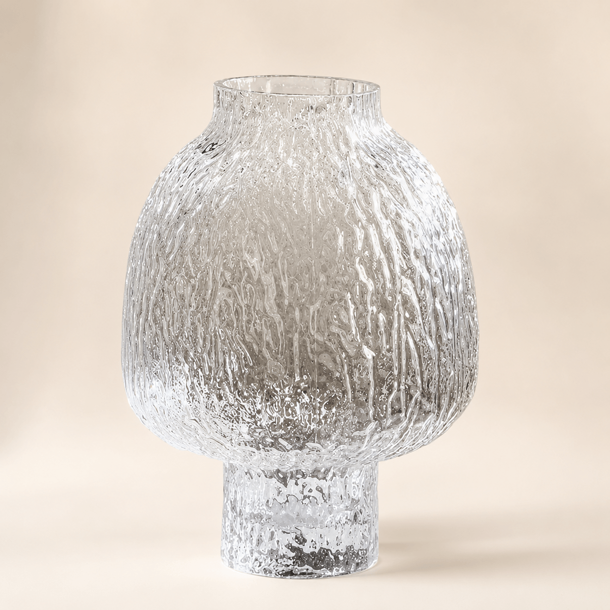 Clear textured glass vase with a rounded lantern body and raised pedestal base on a warm ivory background
