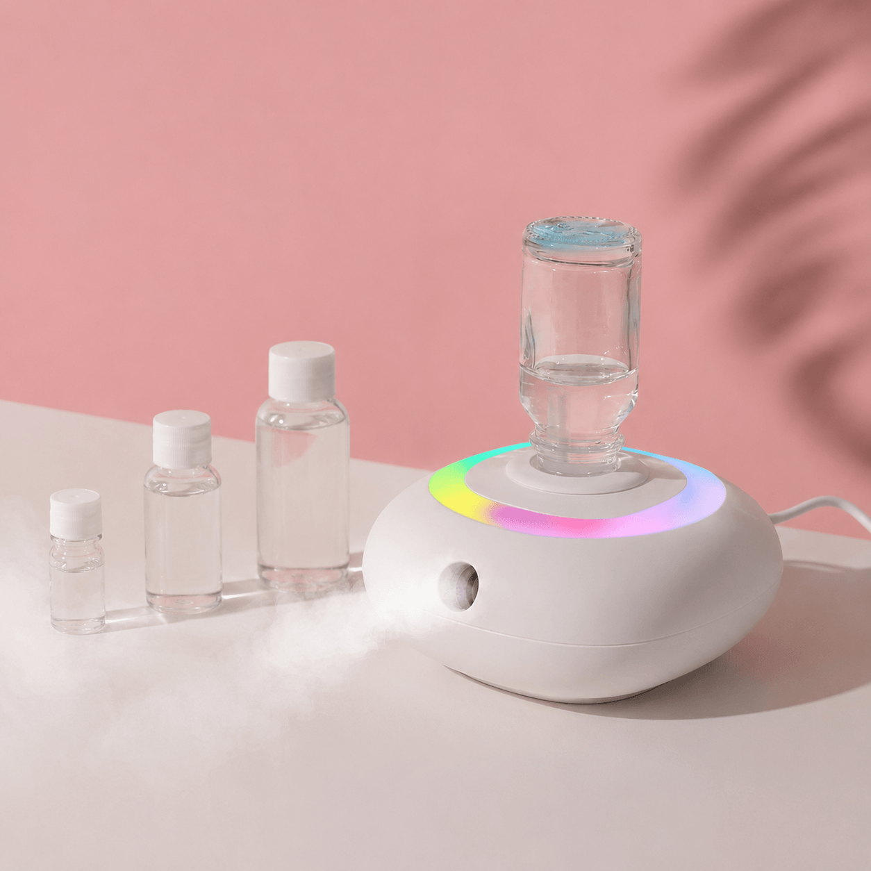Rainbow diffuser on a pink desktop with essential oil bottles and soft mist