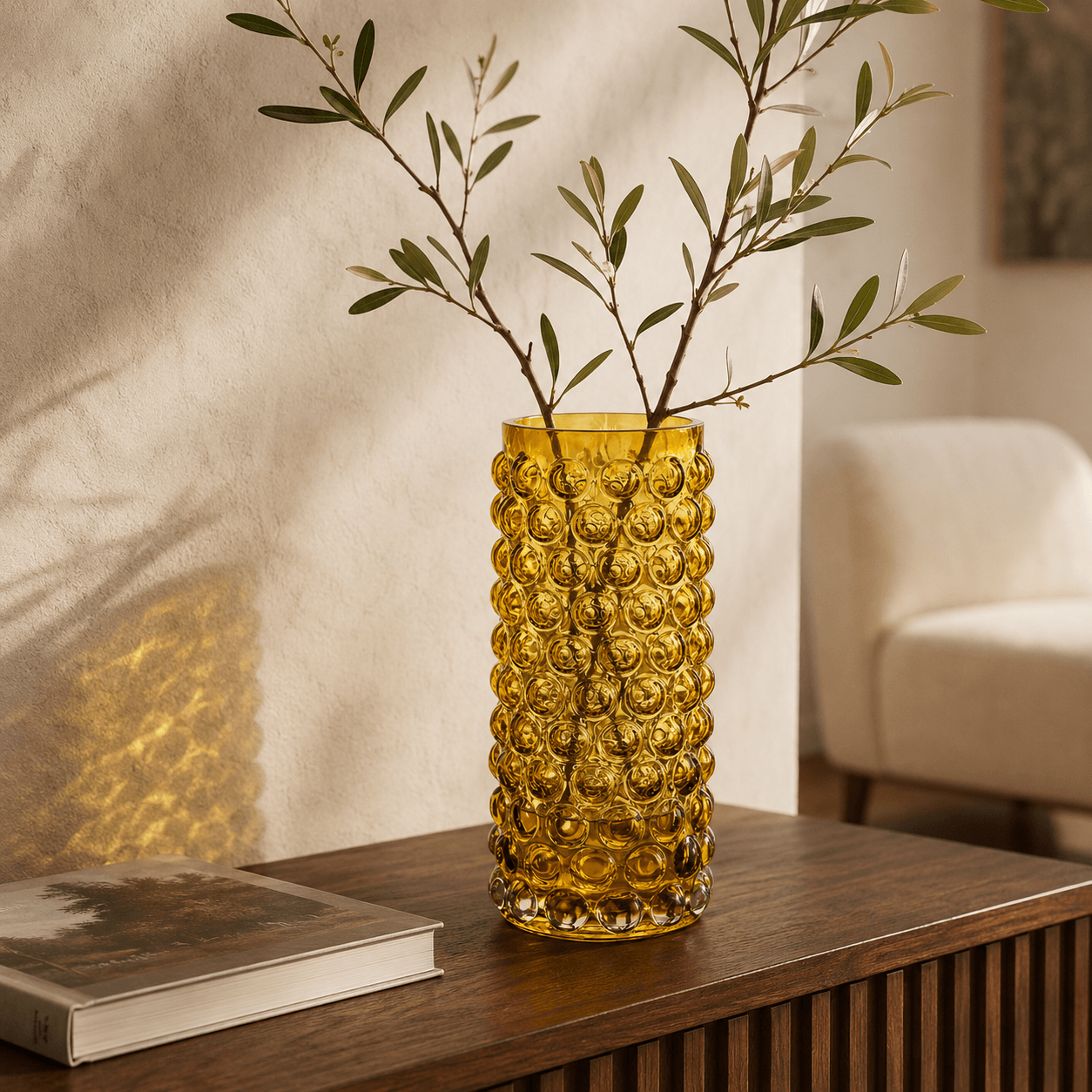 Amber tall bubble glass vase holding leafy branches on a walnut console in a warm living room
