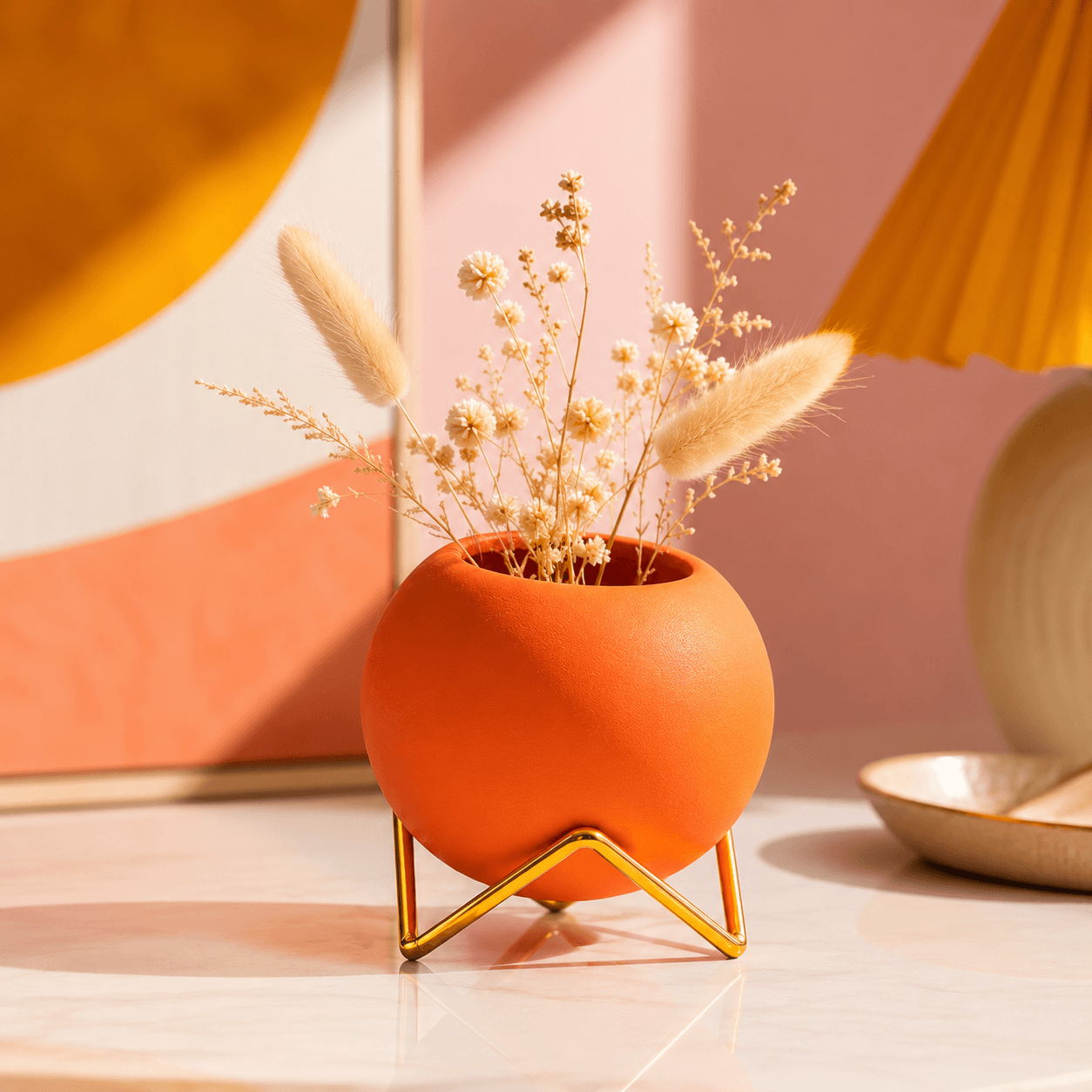 Orange round vase with gold stand and dried floral stems in a warm