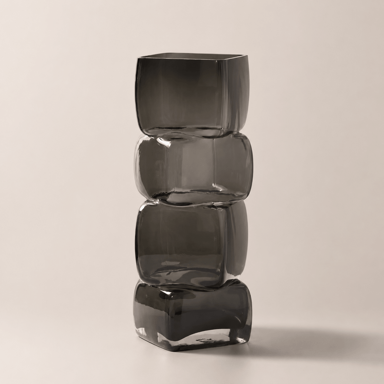 Smoky gray sculptural hand-blown glass vase with stacked geometric form on a clean neutral background.
