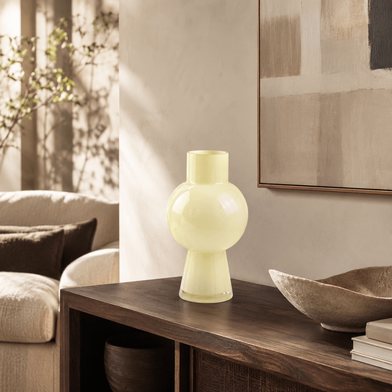 Tall ivory glass vase displayed empty on a dark walnut console in a warm living room