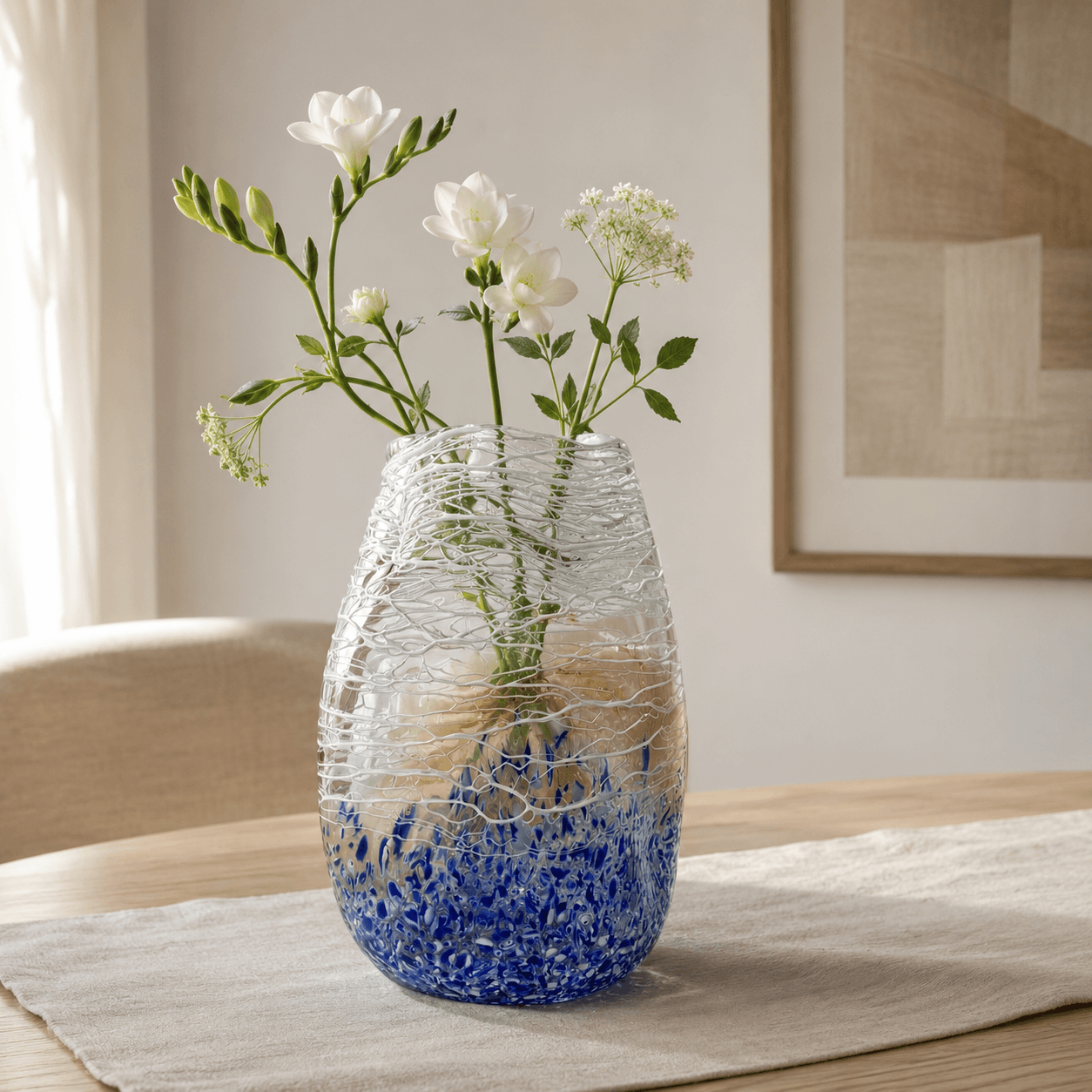 Blue purple textured art glass vase styled with white flowers on a light oak table