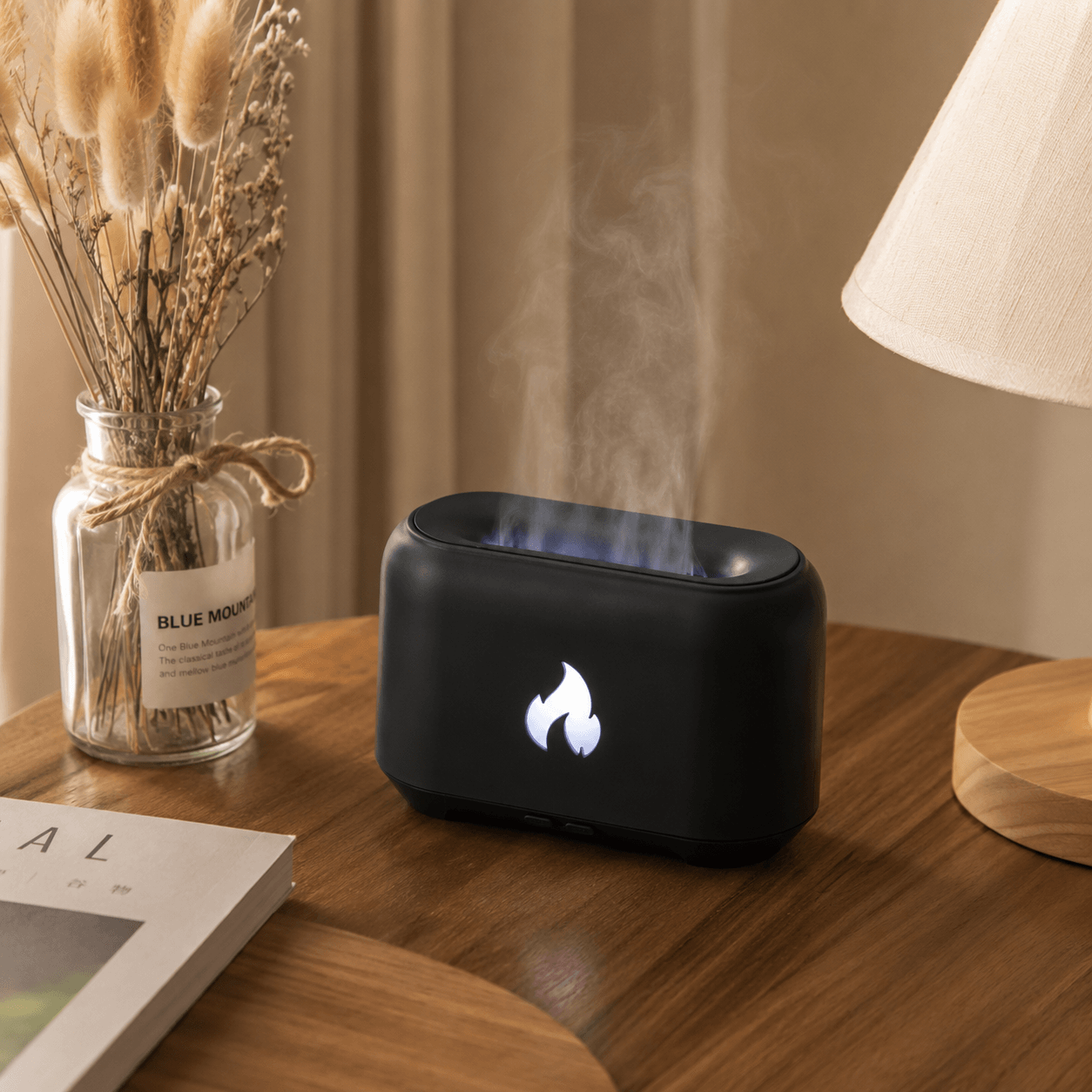 White flame aroma diffuser with soft mist on a glossy table beside dried flowers and essential oil.