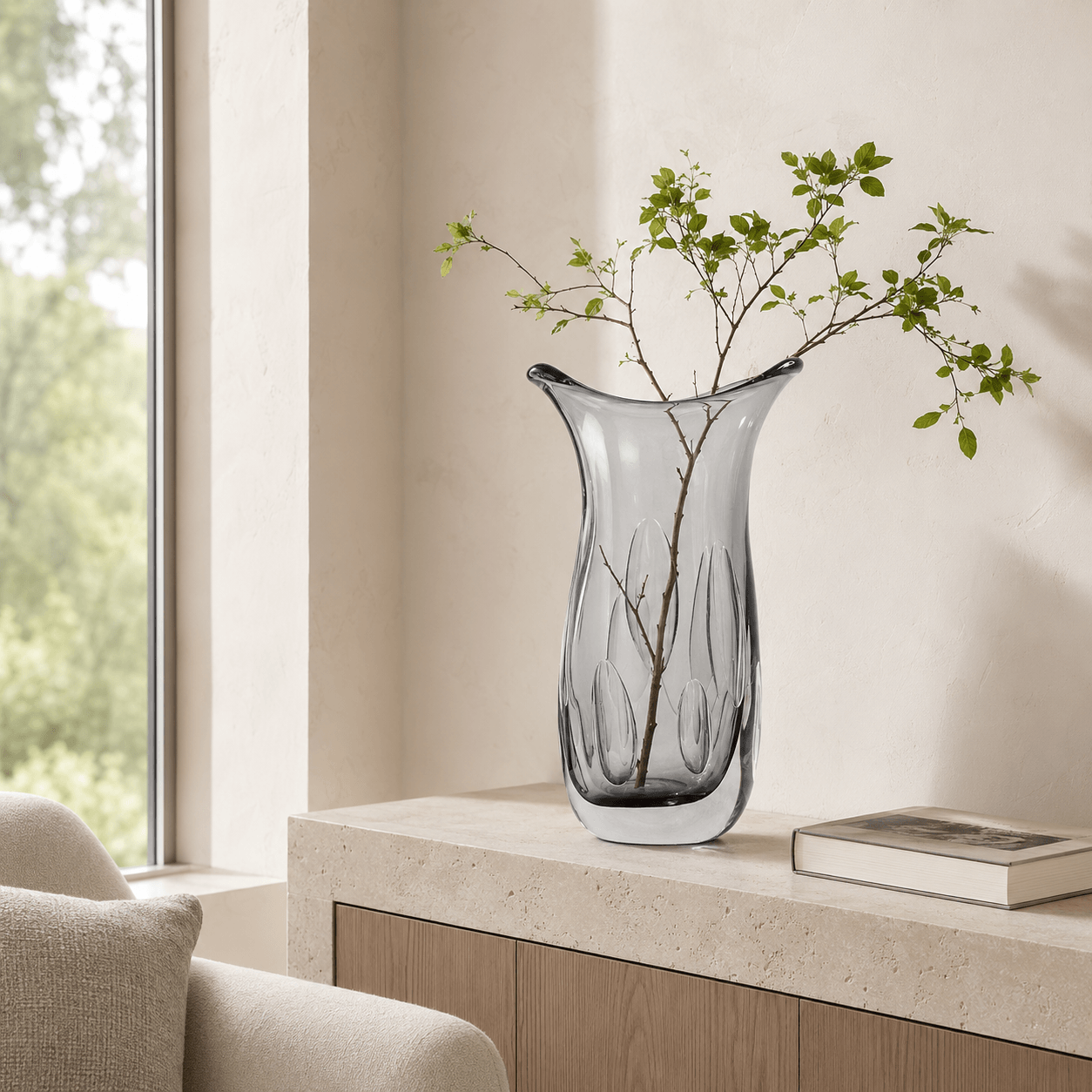 Smoke gray sculptural art glass vase styled on a light stone console in a modern living room