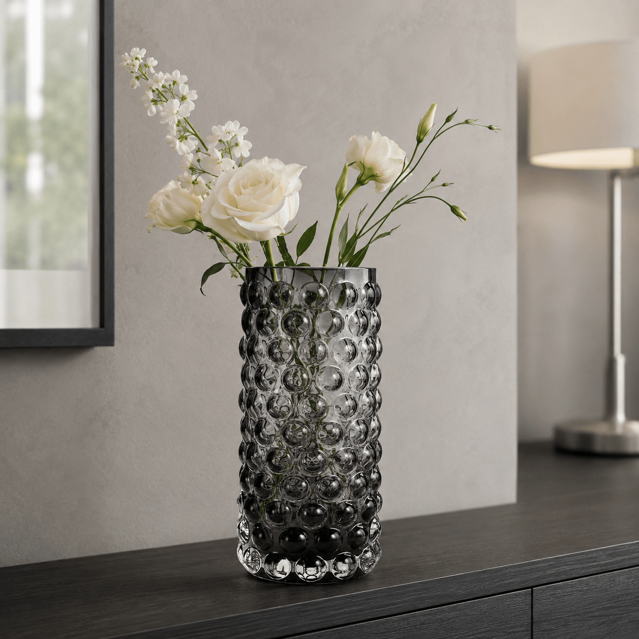 Smoke gray tall bubble glass vase with pale flowers on a dark console in a modern neutral living room
