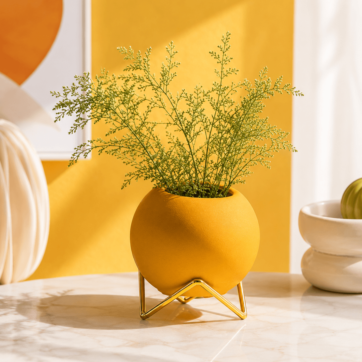 Yellow round vase with gold stand and green foliage in a sunny home decor scene