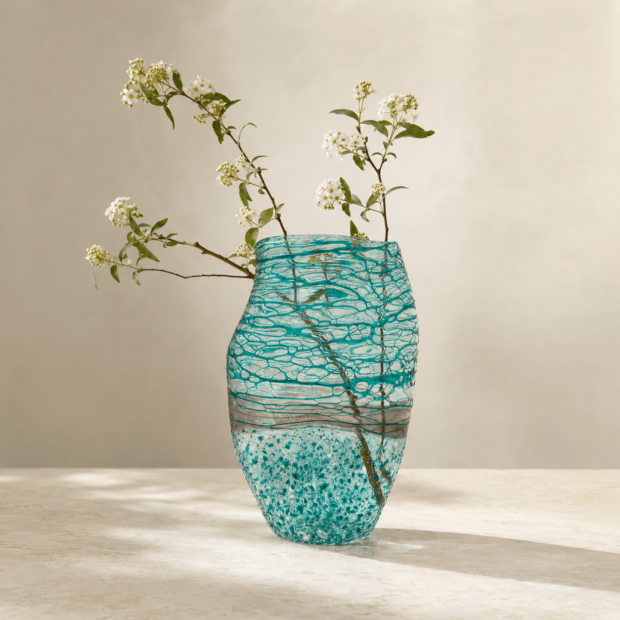 Blue green art glass vase holding fresh branches with layered texture visible