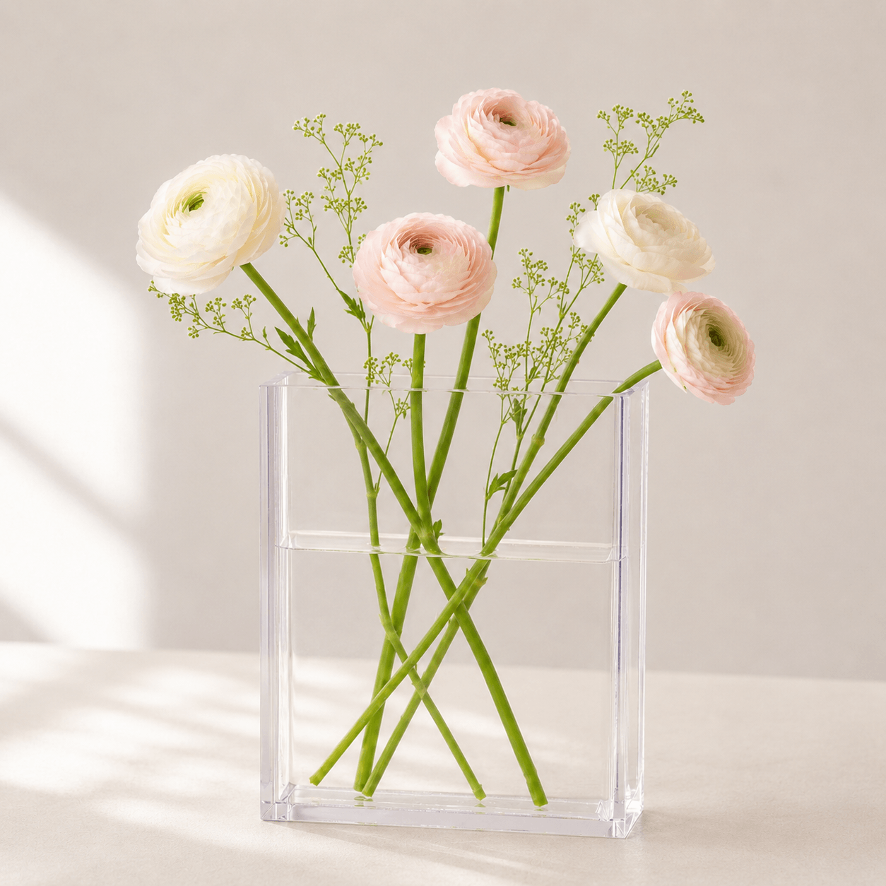 Clear book-shaped vase with blush and ivory flowers in soft natural light.