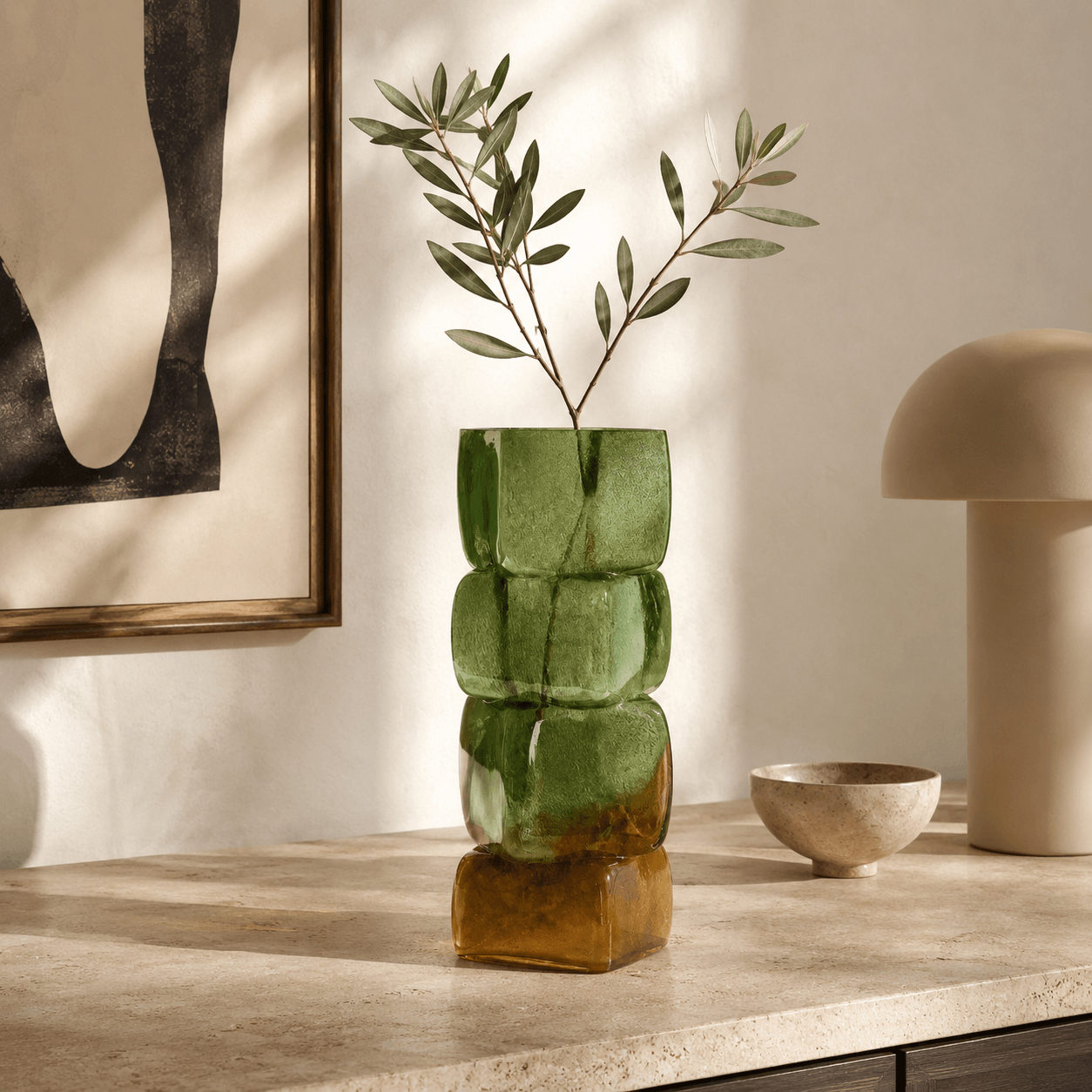 Olive amber sculptural glass vase styled with olive branches on a modern stone console table.