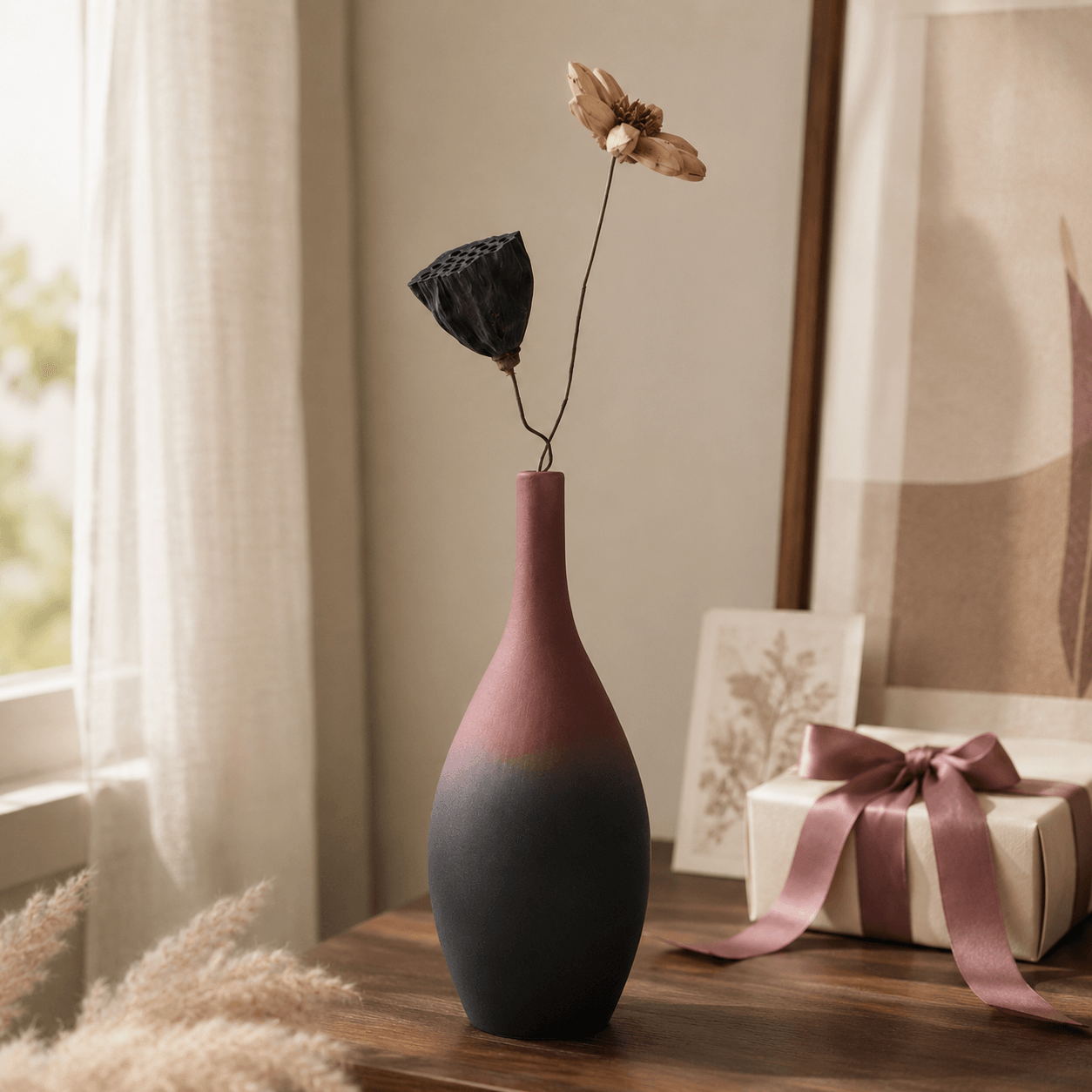 Tall mauve and charcoal bottle vase with dried stems beside a gift box