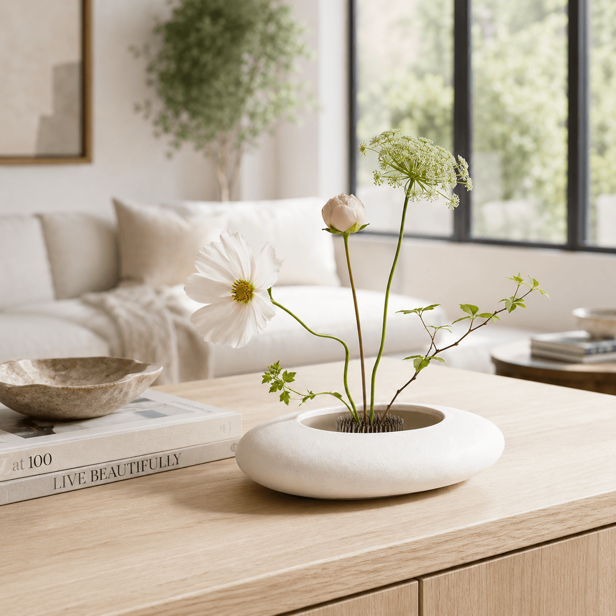 White ceramic flower bowl with a minimalist floral arrangement styled in a bright living room.