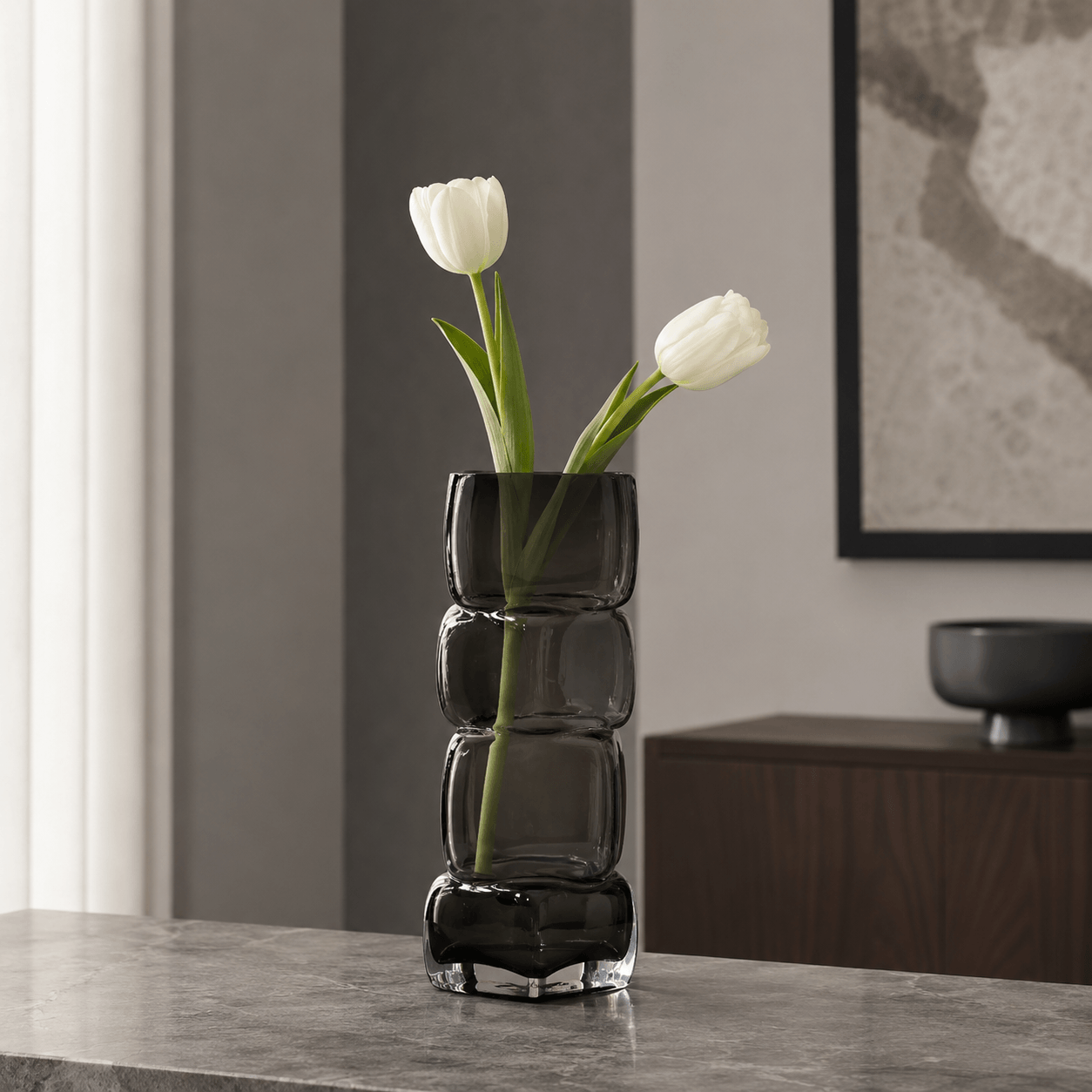 Smoky gray sculptural glass vase with white tulips in a modern neutral interior.