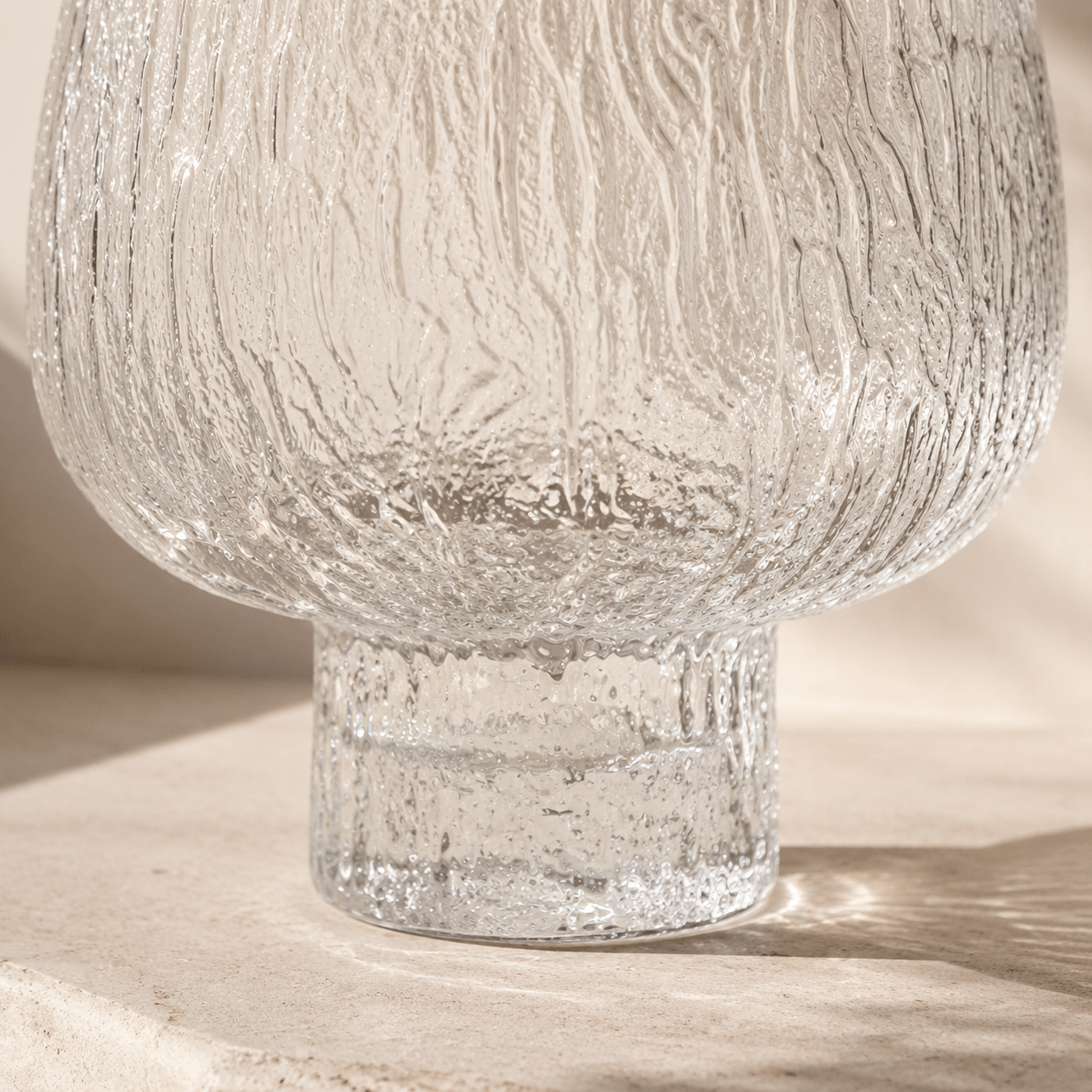 Close detail of the rounded clear glass body and raised textured pedestal base in natural light
