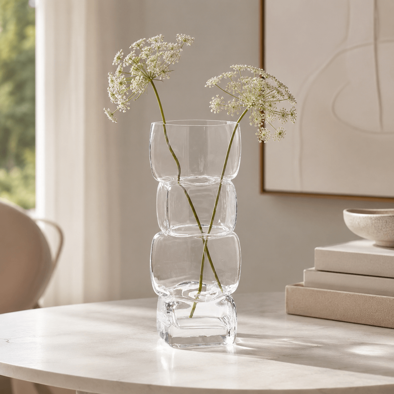 Crystal clear sculptural glass vase with delicate white flowers on a bright round table.