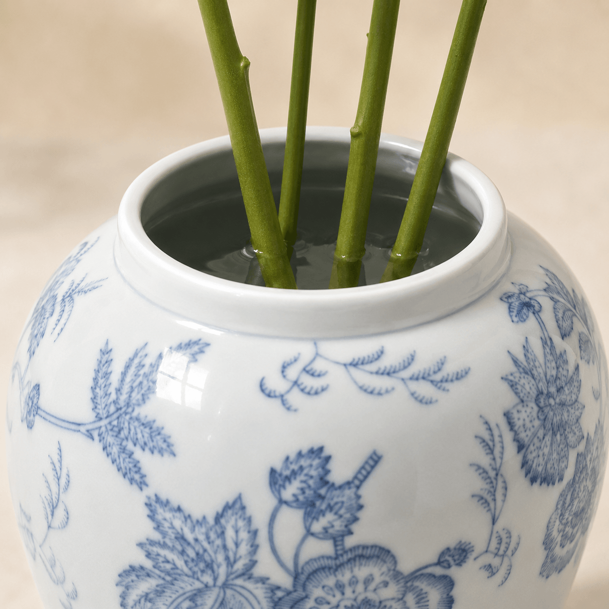 Glazed blue and white ceramic vase filled with water and fresh green flower stems