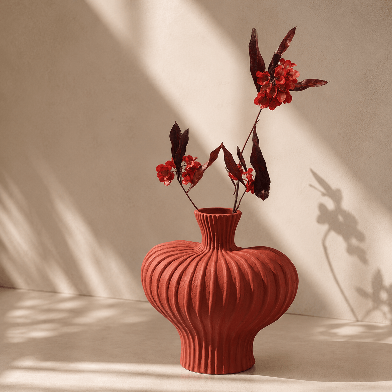 Terracotta Red ribbed ceramic vase with red floral stems in warm sunlight
