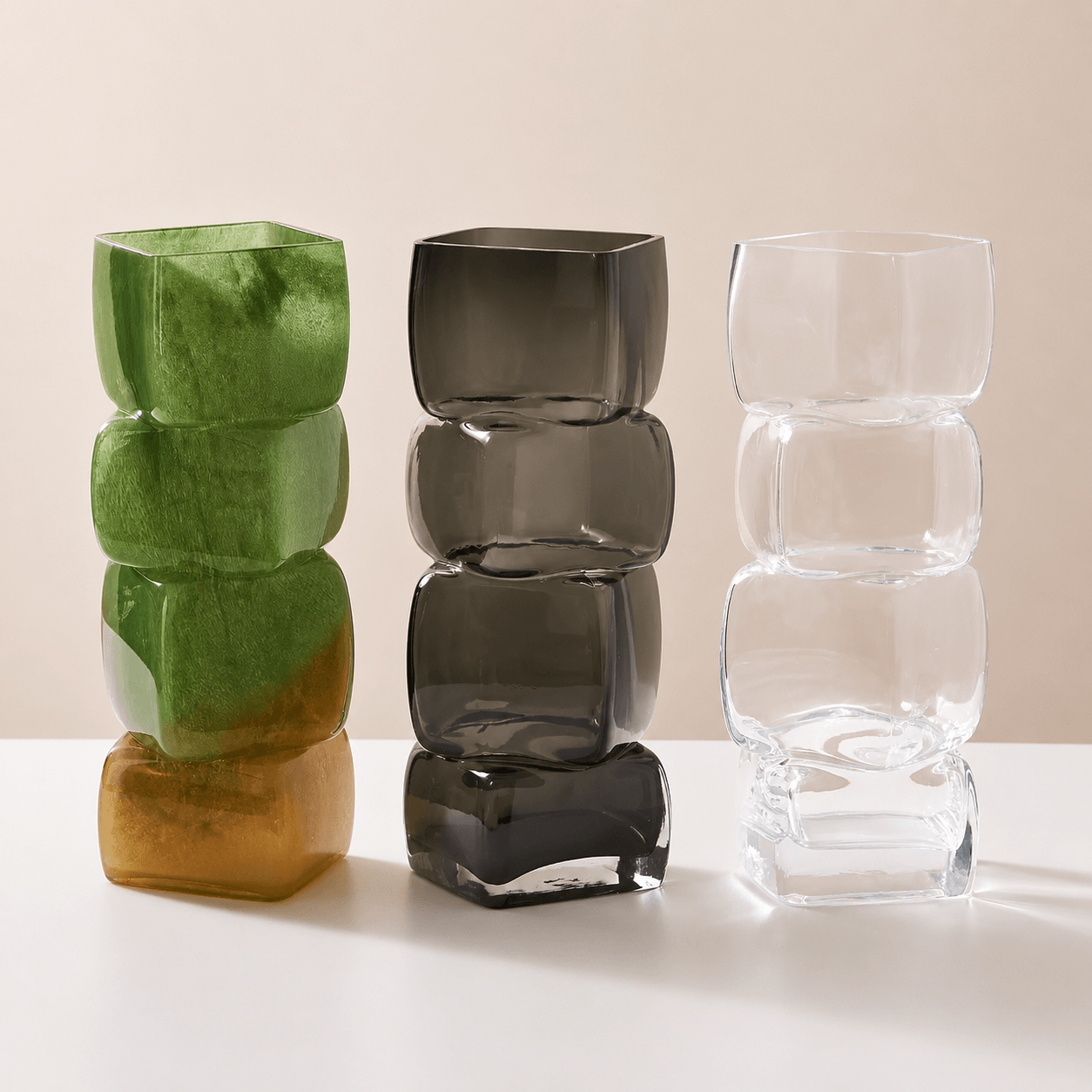 Olive amber, smoky gray, and crystal clear sculptural glass vases displayed together.