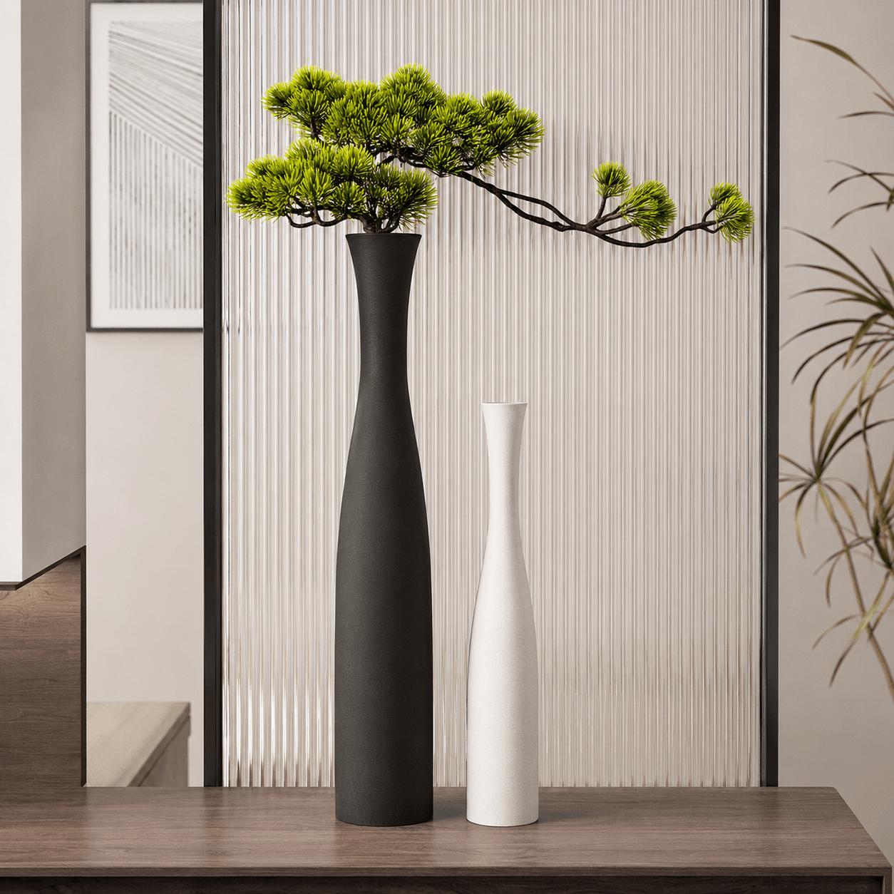 Large matte black vase and small pearl white vase styled with a faux pine branch in a minimalist interior.