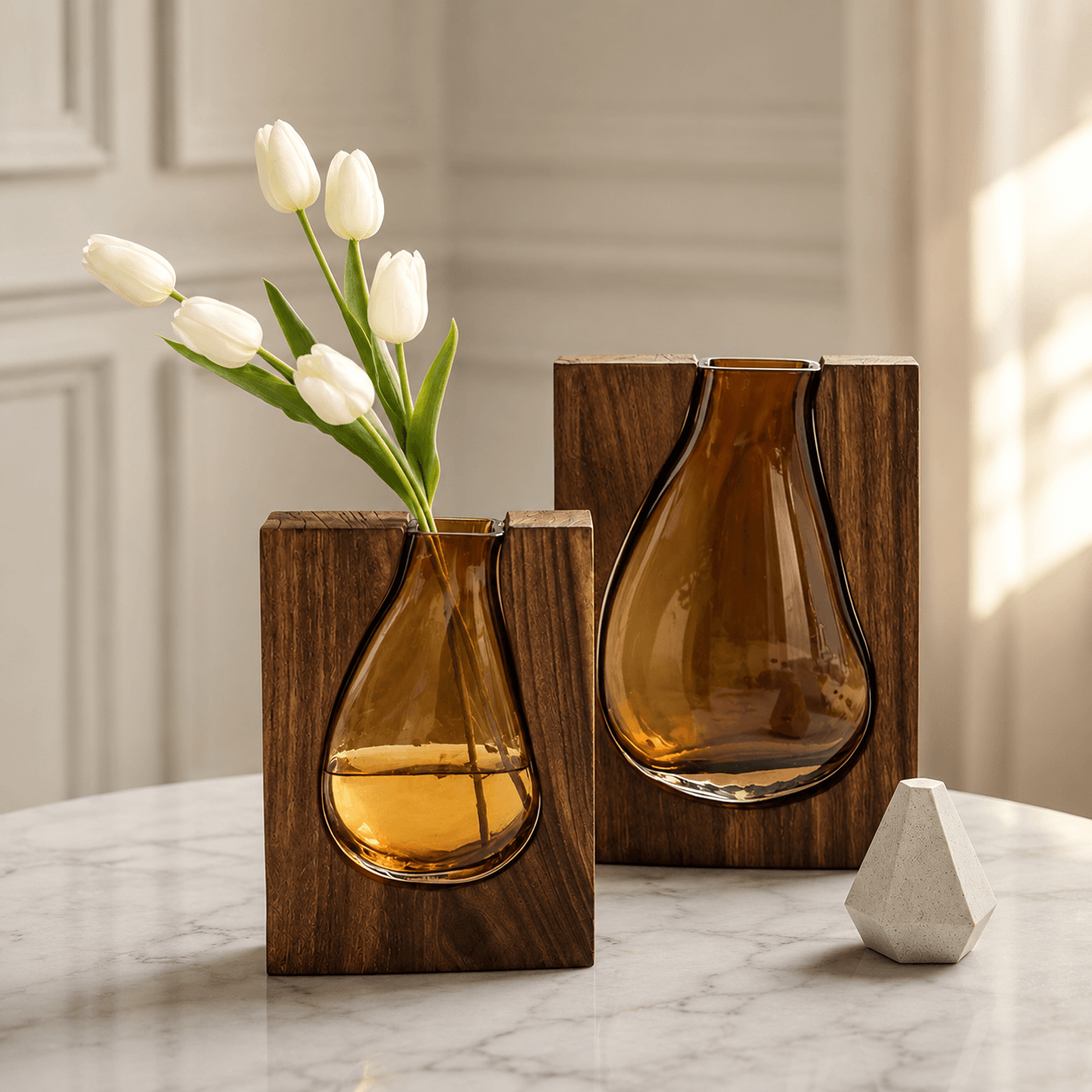 Pair of wooden frame vases with amber glass inserts styled with white tulips on a marble table.